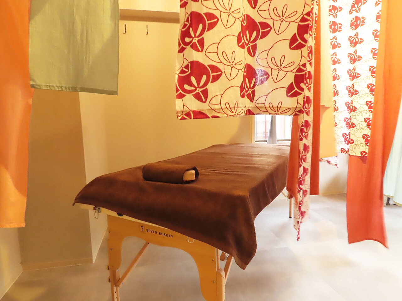 Inside RESET BASE Asakusa, with red floral curtains and a brown treatment bed